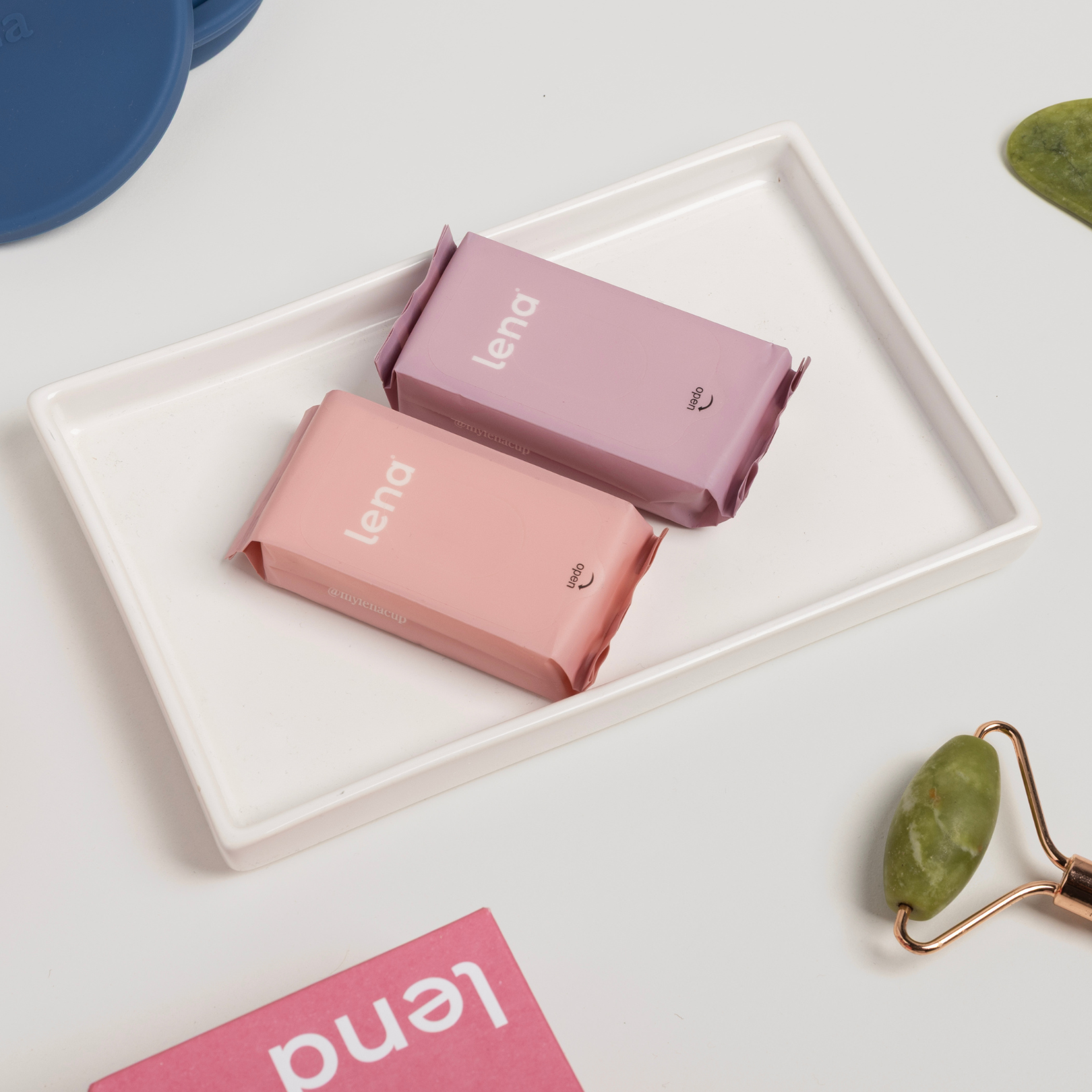 Two pink 'lena' products on a white tray with a blue container and green roller in the background.