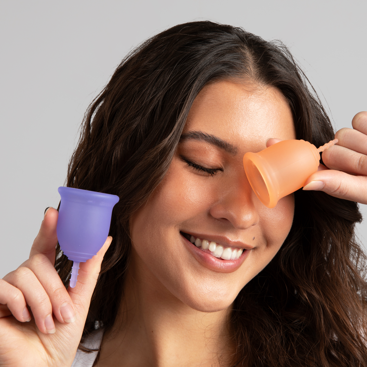 Woman with brown air holding two menstrual cups, one in each hand, eyes closed