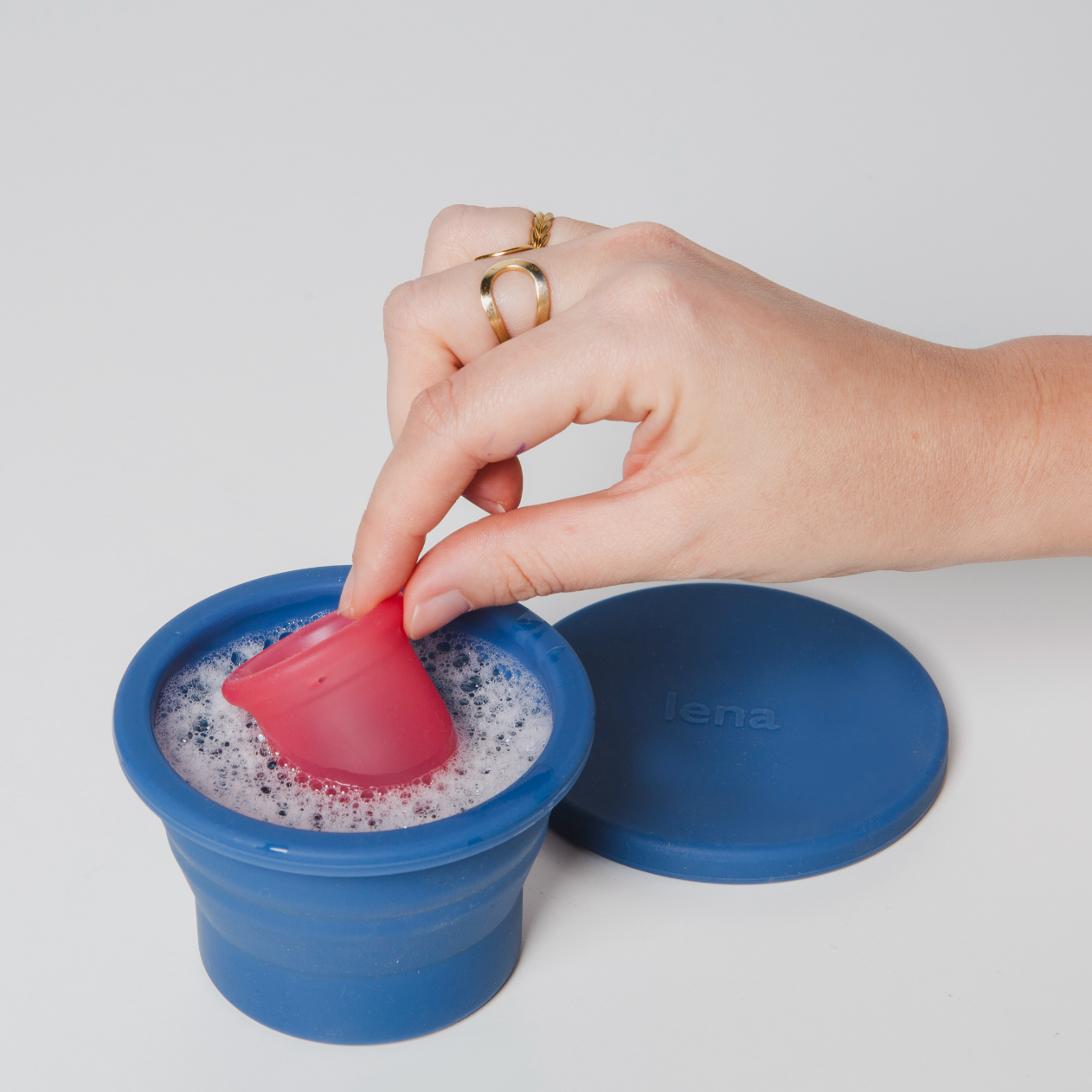 Hand placing a pink silicone lid on a blue collapsible cup with a white background