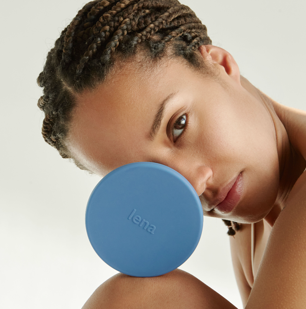 Woman with a Lena Cleaning Container in blue in front of her face. She is looking at the camera, soft cream background