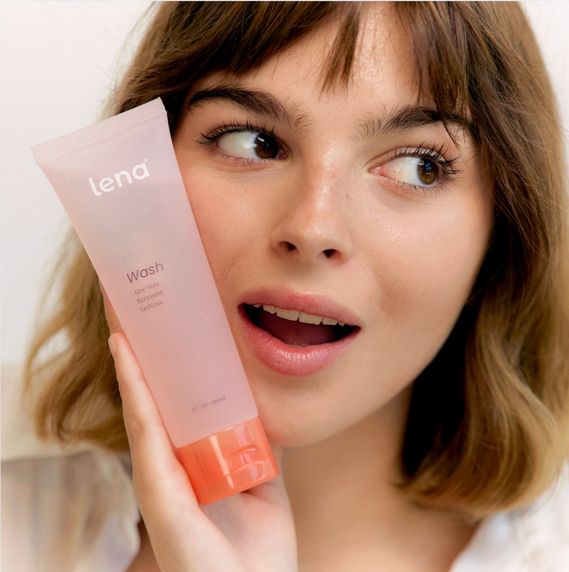 Woman holding a pink Lena Wash tube against a neutral background