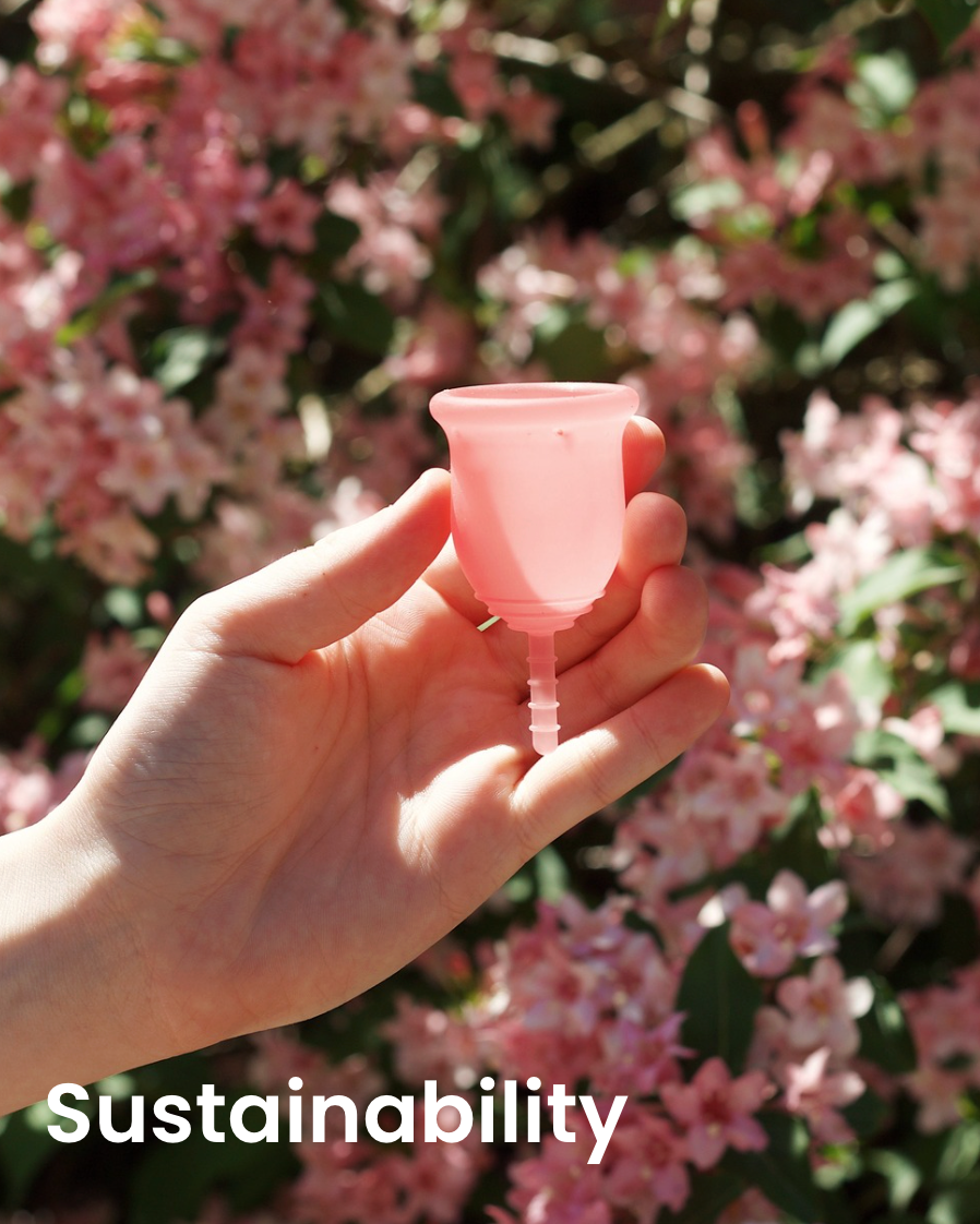 Hand holding a pink menstrual cup with a blurred floral background and 'Sustainability' text.