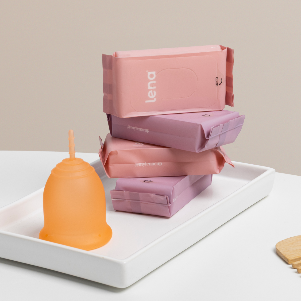 Stack of pink Lena products on a white tray with an orange candle.