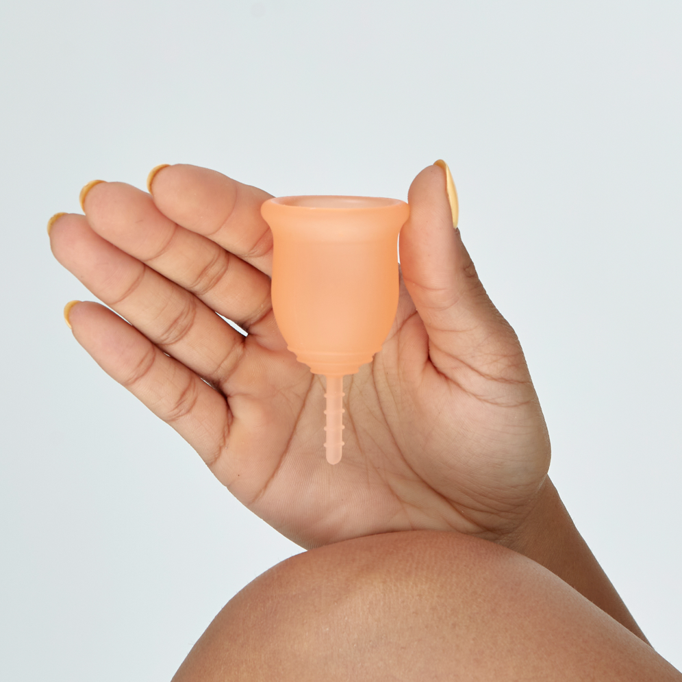 Hand holding a menstrual cup with a light gray background