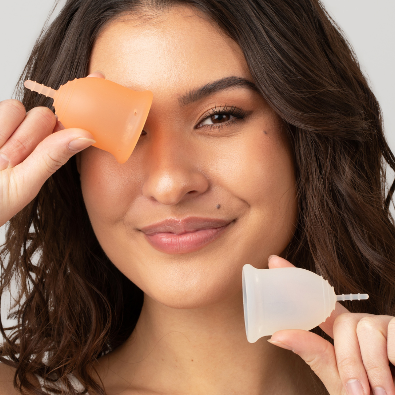 Woman holding two menstrual cups close to her face against a neutral background