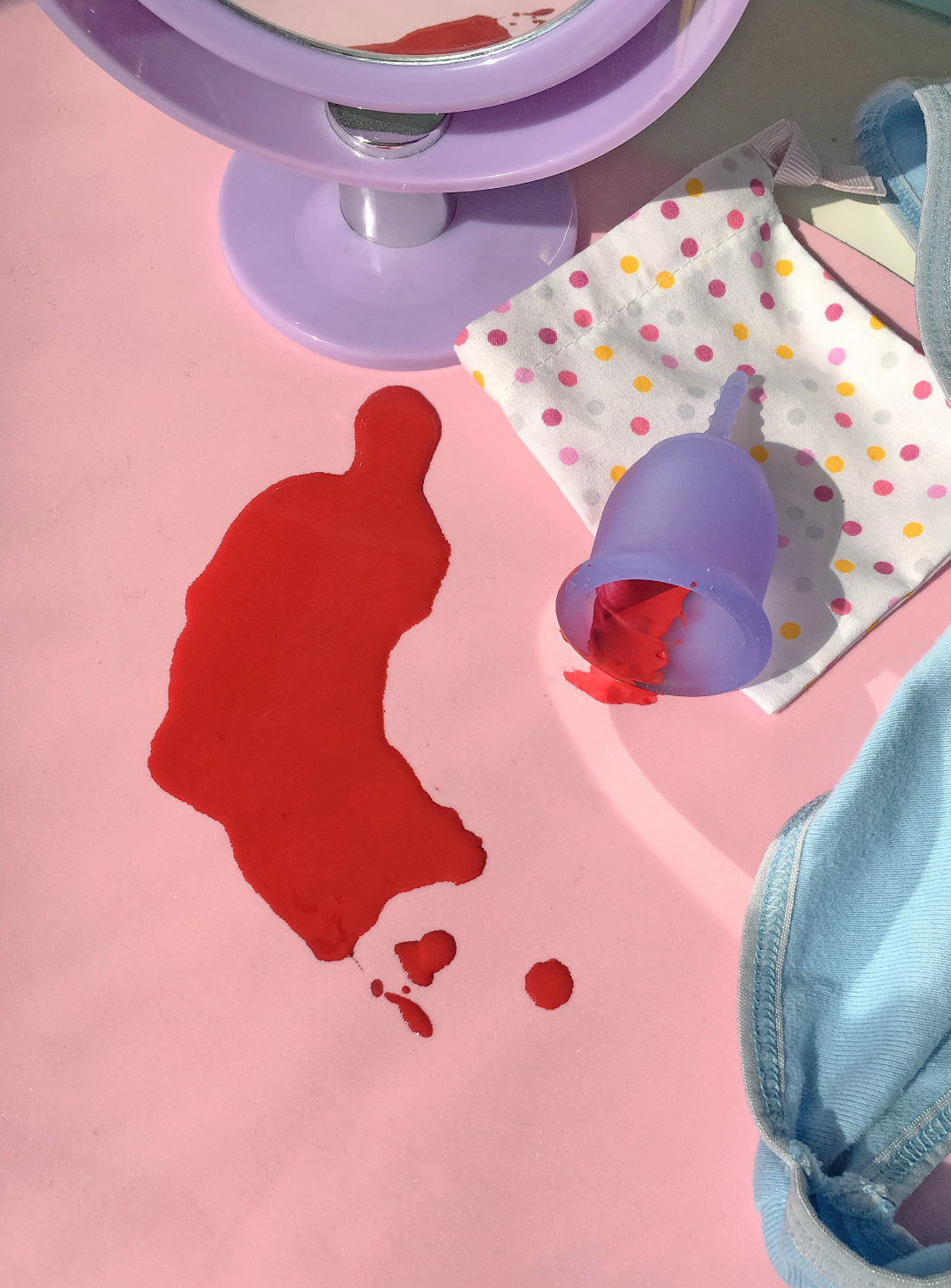 Purple Lena Cup with red liquid spill on a pink surface