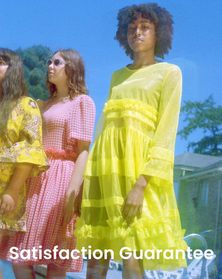Three women in colorful dresses standing outdoors with a 'Satisfaction Guarantee' text overlay.